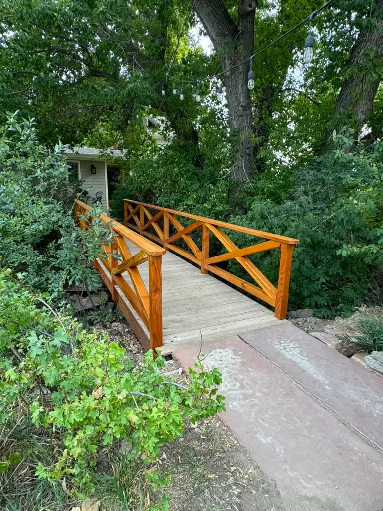 Wooden footbridge with string lights beneath mature trees at Bloom & Brisket